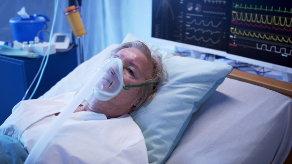 Covid-19 infected patient with oxygen mask in bed in hospital, looking at camera. Coronavirus and breathing problems concept.