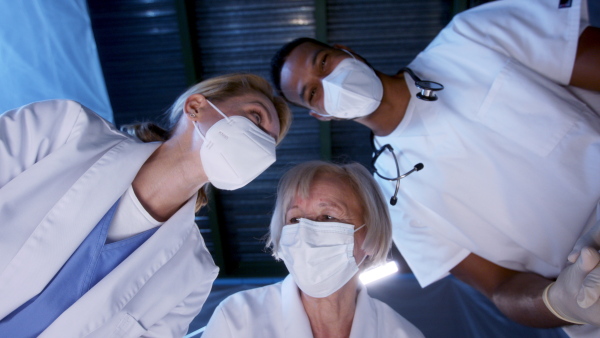 Bottom view of cheerful doctors leaning over covid-19 patient n hospital, clapping. Coronavirus and recovery concept.