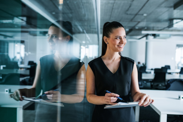 Young businesswoman with clipboard in an office, standing. Copy space.