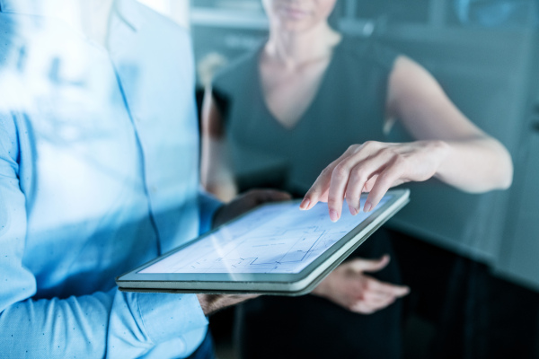 Midsection of young unrecognizable businesspeople with tablet in an office, working. Shot through glass.