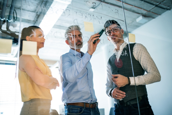 A front view of group of business people standing in an office, brainstorming. Shot through glass.