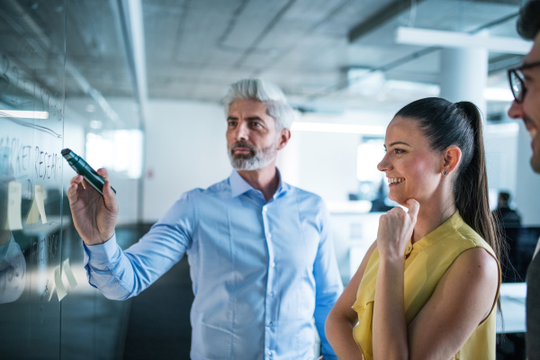 A side view of group of business people standing in an office, brainstorming.