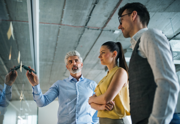 A side view of group of business people standing in an office, brainstorming.