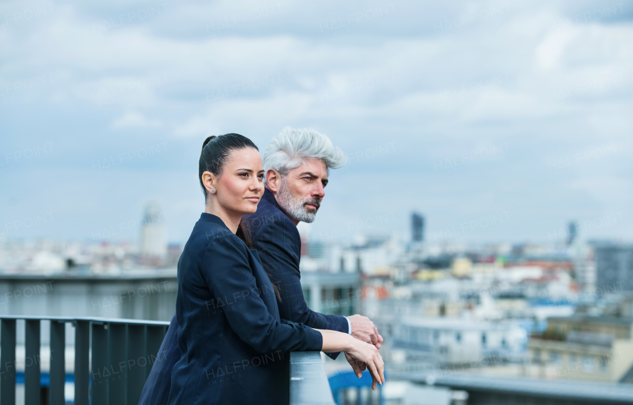 A mature businessman and young businesswoman standing on a terrace, talking.