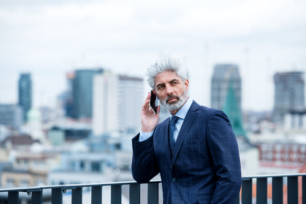 A portrait of mature businessman with smartphone standing on a terrace, working.