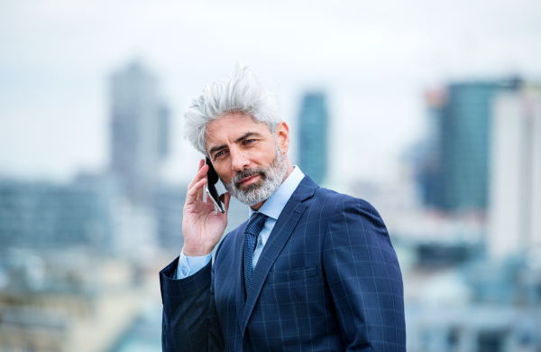 A portrait of mature businessman with smartphone standing on a terrace, working.