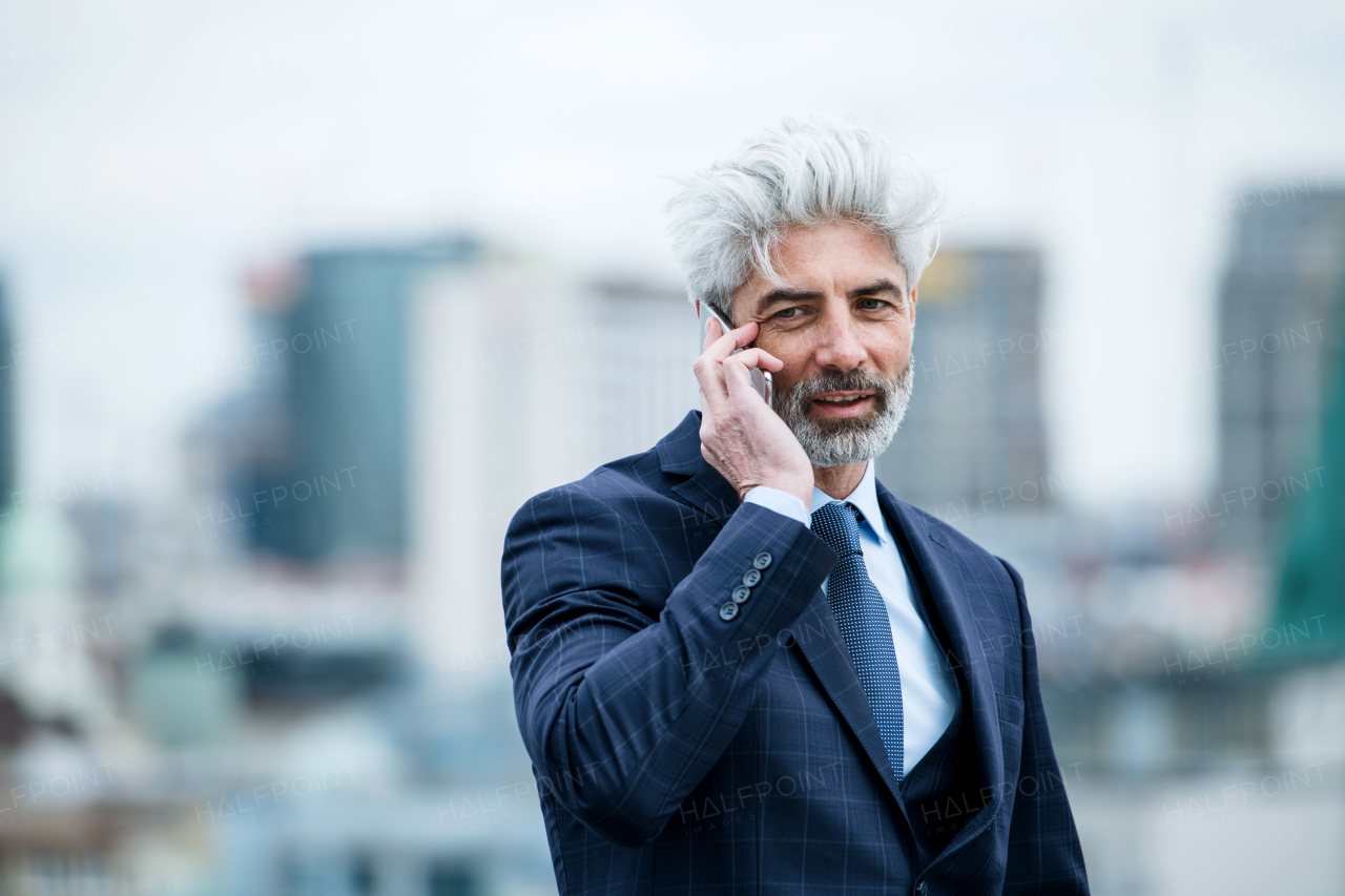 A portrait of mature businessman with smartphone standing on a terrace, working.