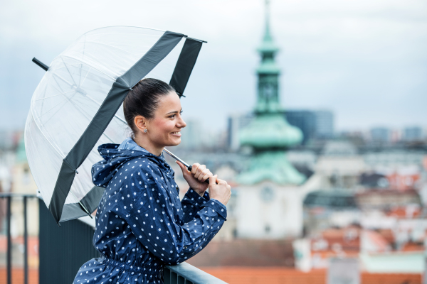 A young woman with umbrella and anorak standing on a terrace, resting