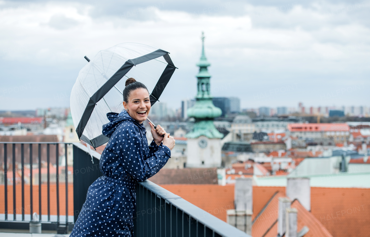 A young woman with umbrella and anorak standing on a terrace, resting.