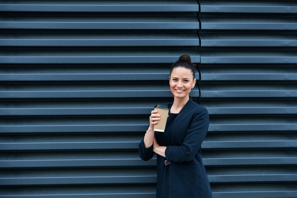 A businesswoman with coffee standing on a terrace, looking at camera. Copy space.