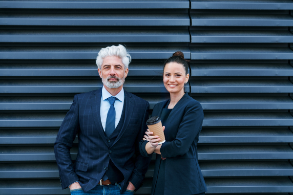 A mature businessman and young businesswoman standing on a terrace, looking at camera.