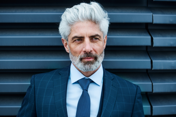 A front view of mature businessman standing outdoors against dark background.