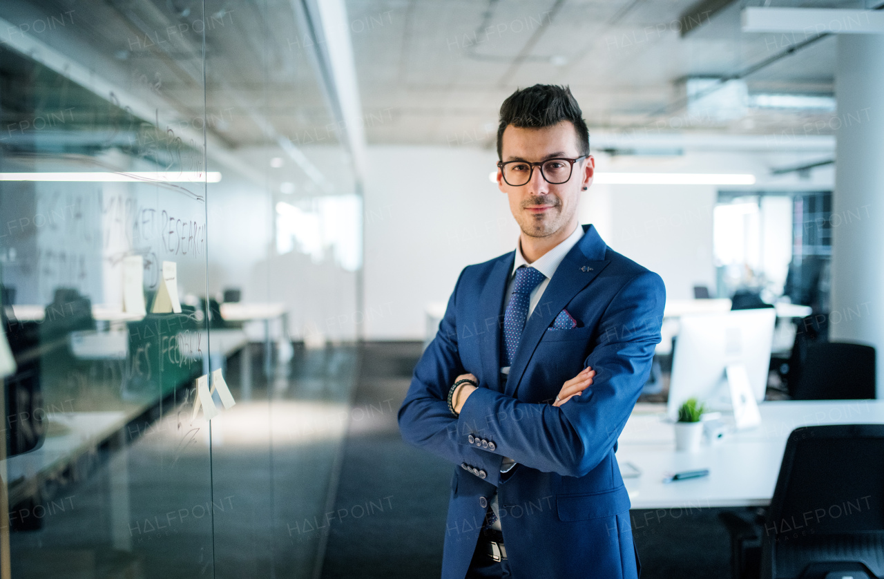 A portrait of young businessman standing in an office, arms crossed. Copy space.