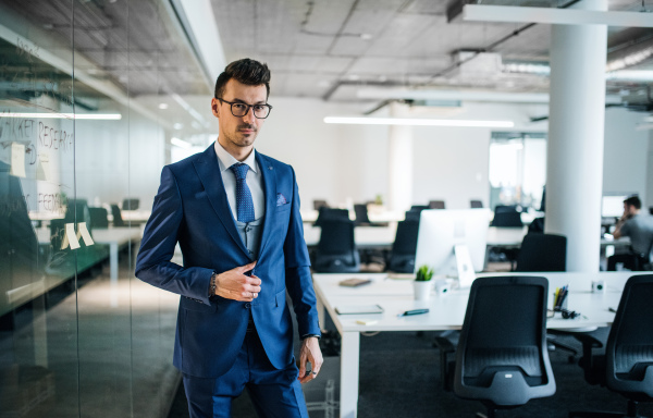 A portrait of young businessman standing in an office, looking at camera. Copy space.