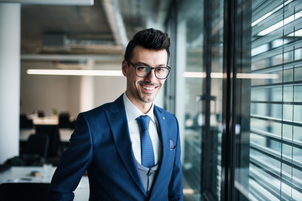 A portrait of young businessman standing in an office, looking at camera. Copy space.