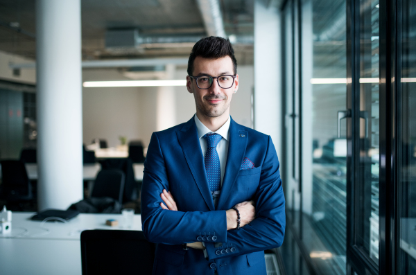 A portrait of young businessman standing in an office, looking at camera. Copy space.