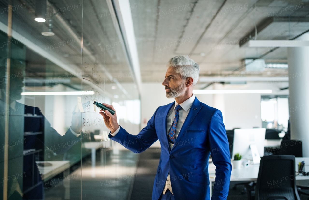 A portrait of mature businessman standing in an office, brainstorming.