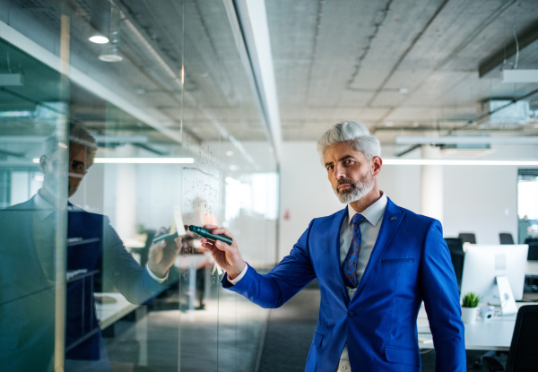 A portrait of mature businessman standing in an office, brainstorming.