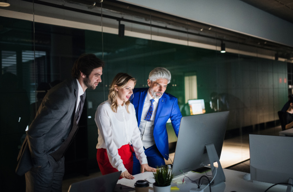 A group of businesspeople in an office in the evening or at night, using computer.