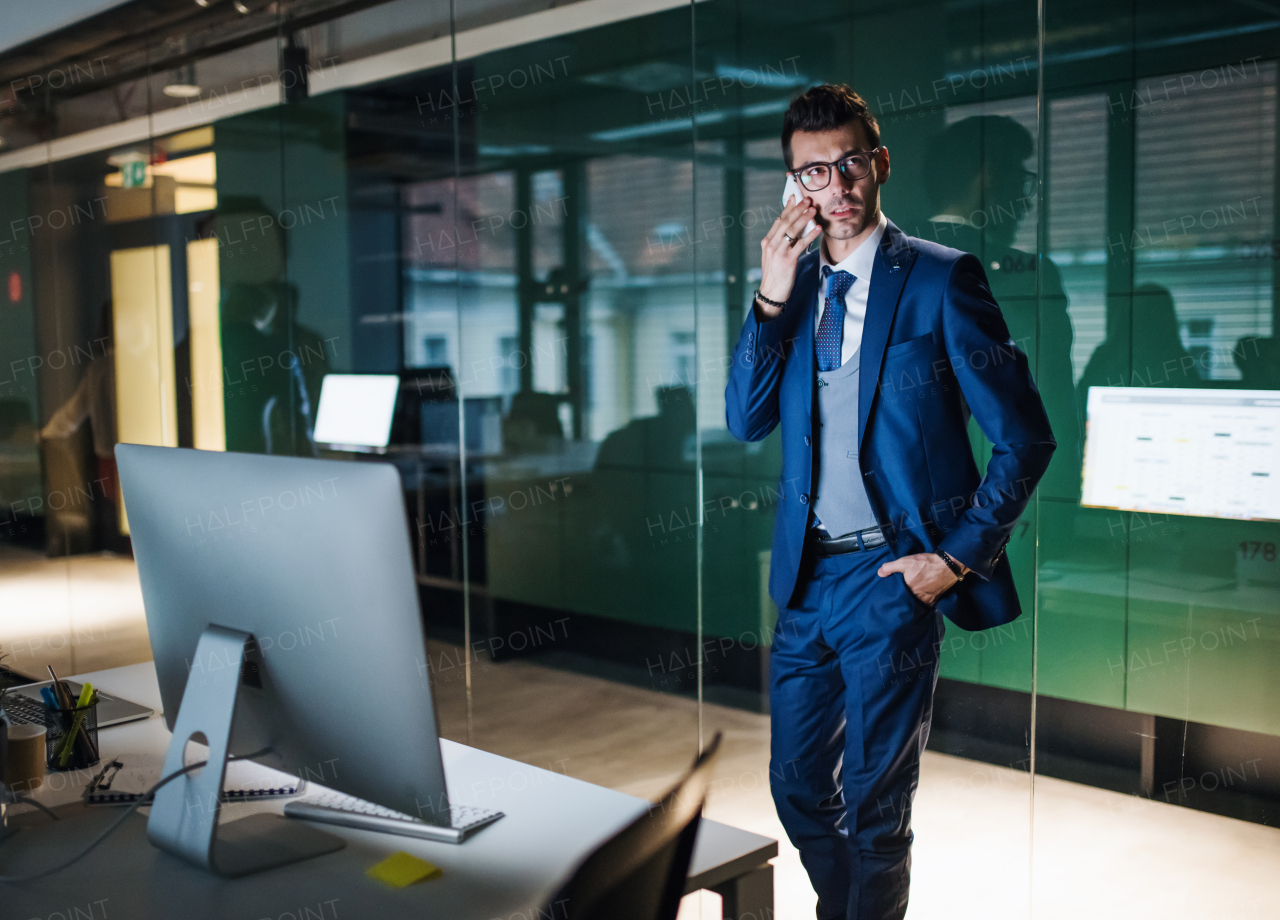 A portrait of young businessman with smartphone and laptop standing in an office. Copy space.