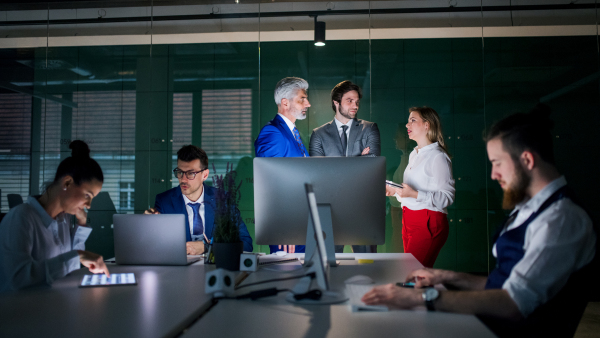 A group of business people in an office in the evening or at night, using computer.