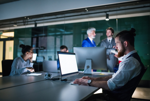 A group of business people in an office in the evening or at night, using computer.