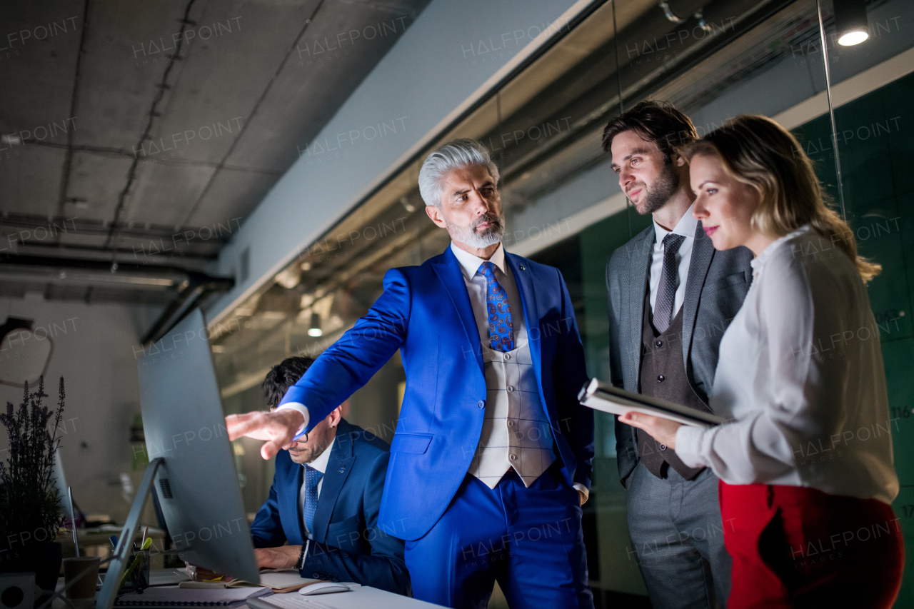 A group of business people in an office in the evening or at night, using computer.