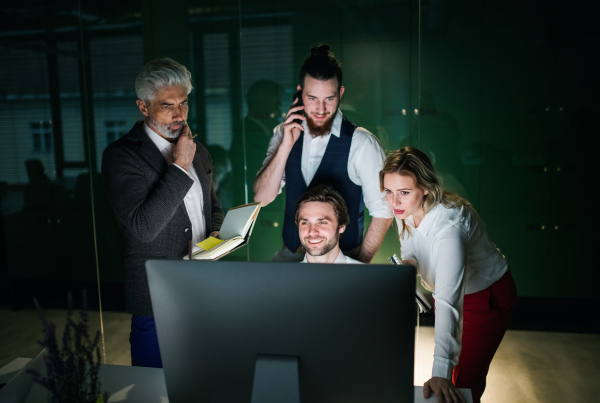 A group of business people in an office in the evening or at night, using computer.