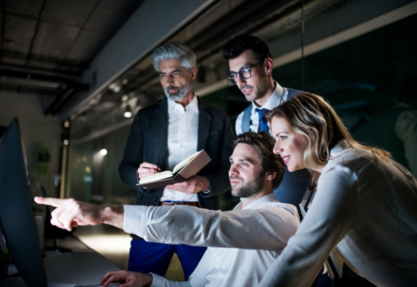 A group of business people in an office in the evening or at night, using computer.