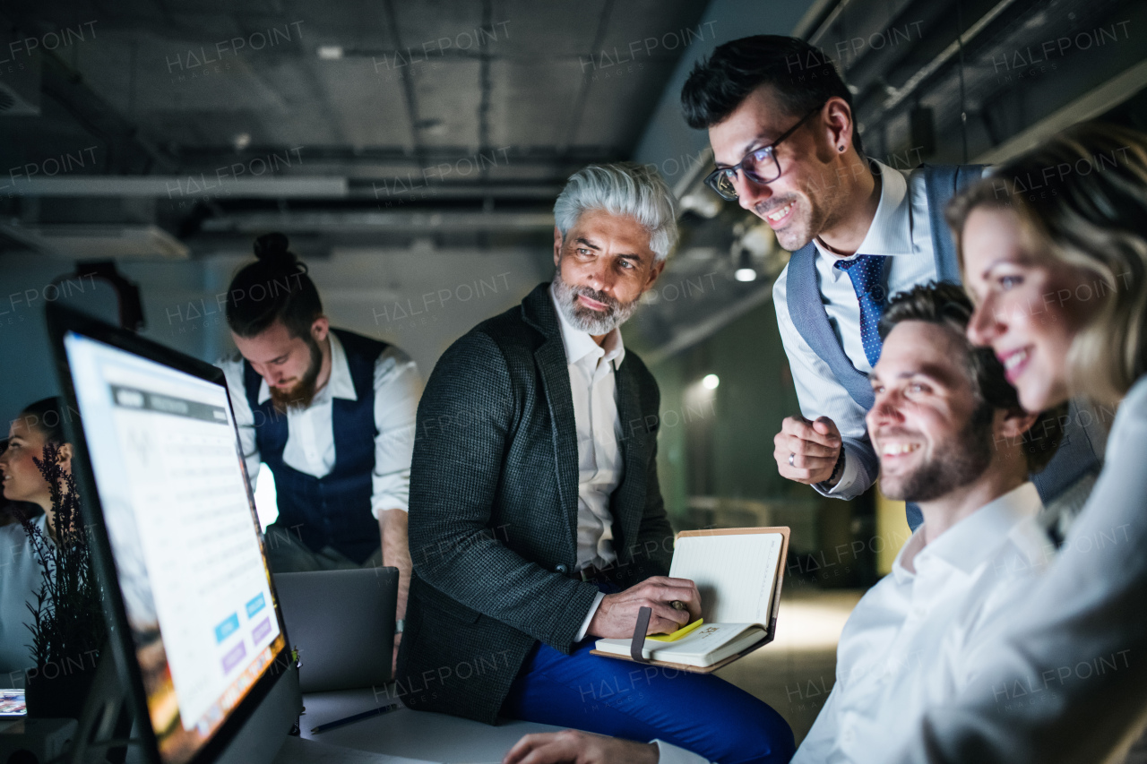 A group of business people in an office in the evening or at night, using computer.