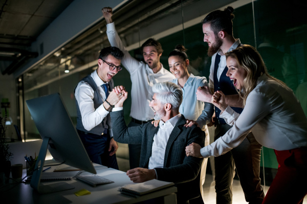 A group of business people with computer in an office in the evening, expressing excitement.