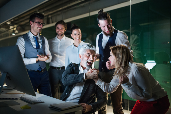 A group of business people with computer in an office in the evening, expressing excitement.