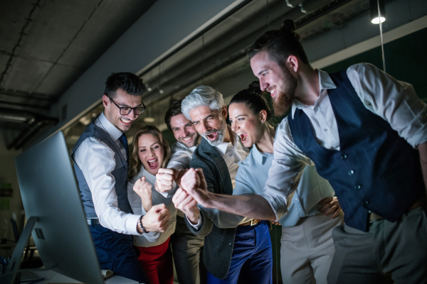 A group of business people with computer in an office in the evening, expressing excitement.