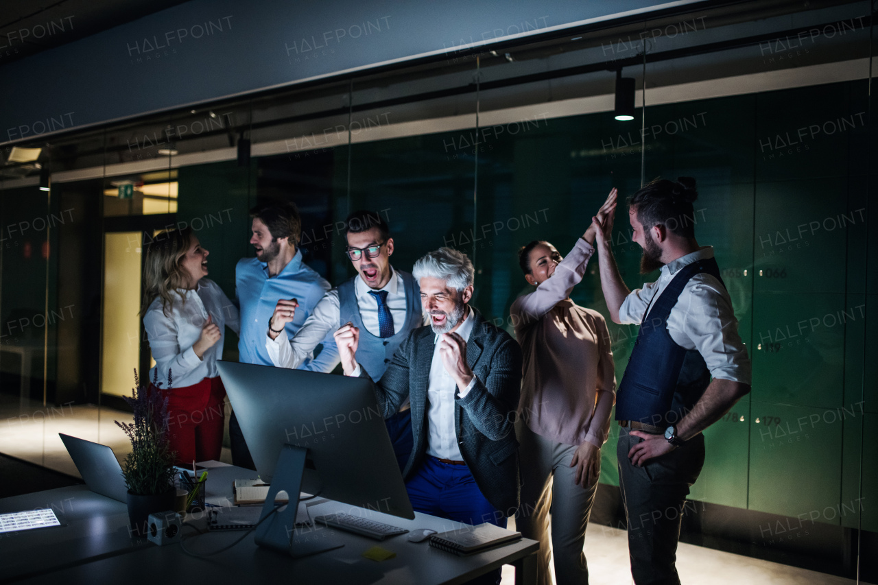 A group of business people with computer in an office in the evening, expressing excitement.