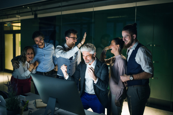 A group of business people with computer in an office in the evening, expressing excitement.