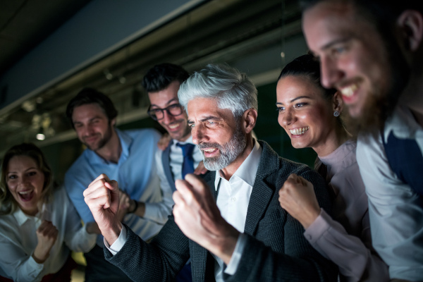 A group of business people with computer in an office in the evening, expressing excitement.