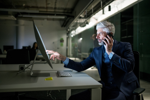 A portrait of mature businessman with smartphone and computer in an office, working.