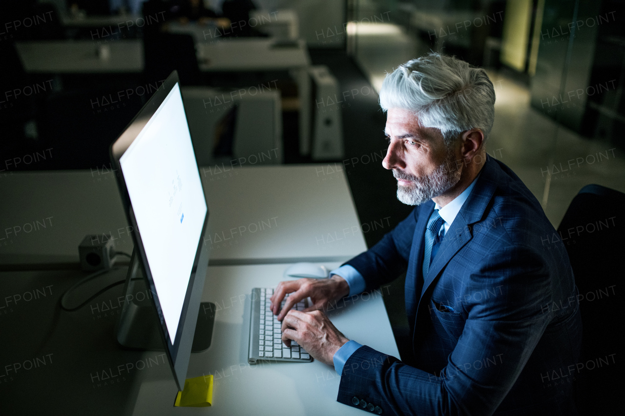 A portrait of mature businessman with computer in an office, working.