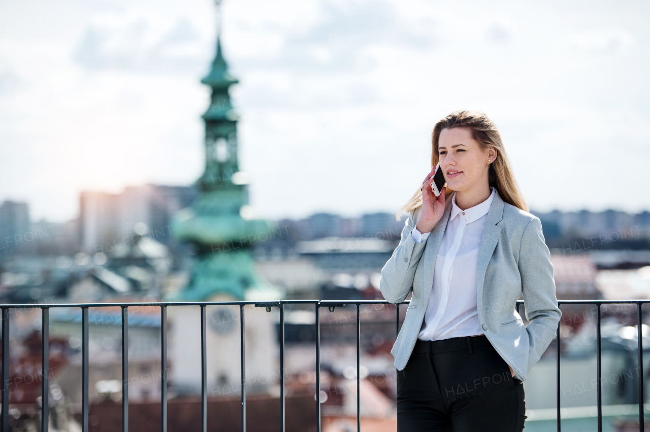 A young businesswoman with smartphone standing on a terrace, making a phone call.