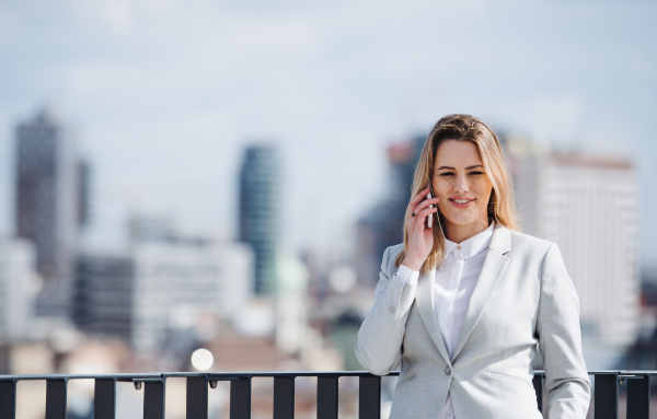 A young businesswoman with smartphone standing on a terrace, making a phone call.