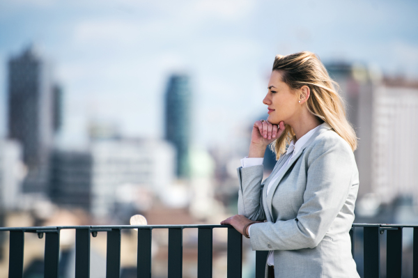 A portrait of young blond businesswoman standing outdoors on terrace outside office. Copy space.