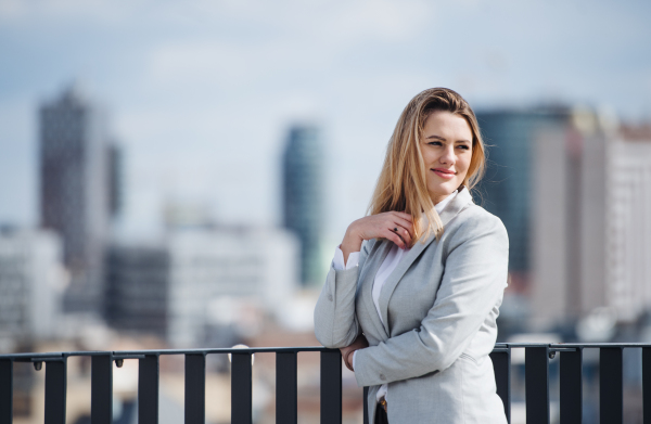 A portrait of young blond businesswoman standing outdoors on terrace outside office. Copy space.