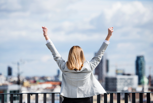 A rear view of young businesswoman standing on a terrace outside office, expressing excitement.