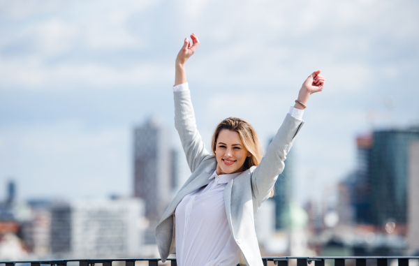 A young businesswoman standing on a terrace outside office, expressing excitement.