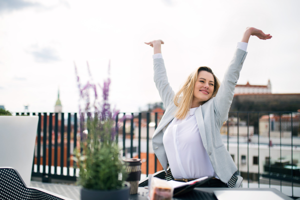 A young businesswoman standing on a terrace outside office, expressing excitement.