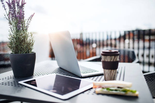 Laptop, tablet, sandwich and coffee on a table on a terrace outside office. Lunch break concept.