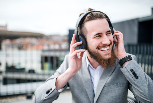 A young businessman with headphones standing on a terrace, listening to music.