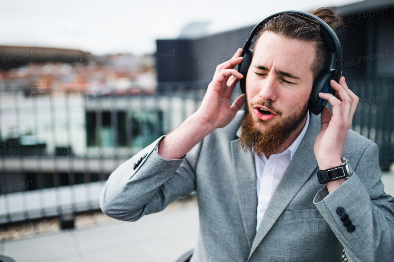 A young businessman with headphones sitting on a terrace, having fun.