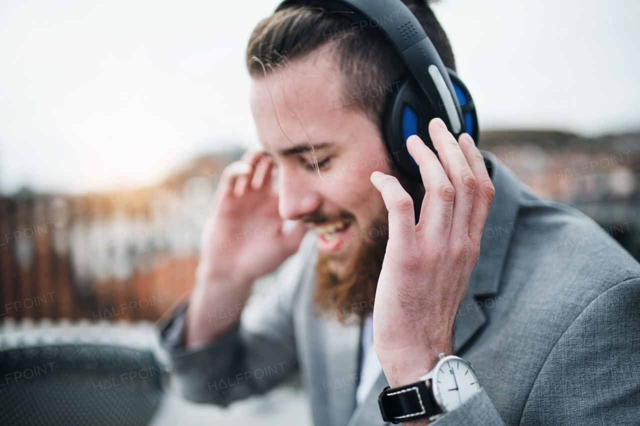 A young businessman with headphones standing on a terrace, listening to music.