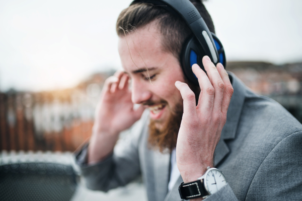 A young businessman with headphones standing on a terrace, listening to music.